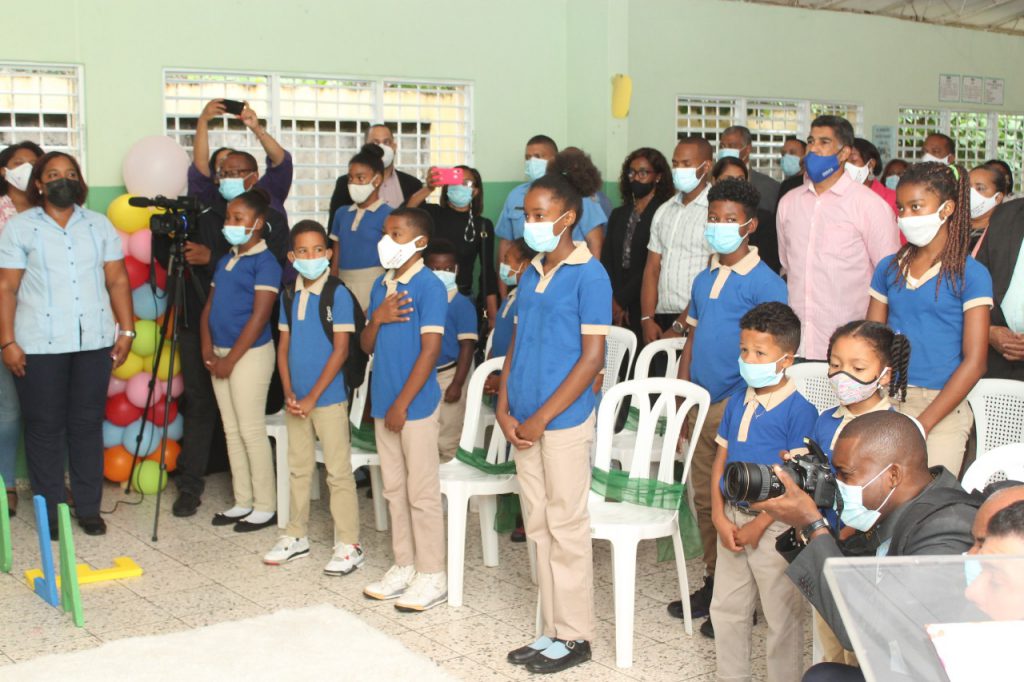 Varios estudiantes de un centro educativo, de pie y utilizando mascarillas, dentro del salón de clases.